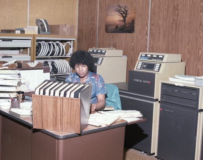 Woman at desk Convair employee surrounded by data in computers and files roughly 1970s courtesy San Diego Air Space Museum on Flickr Commons